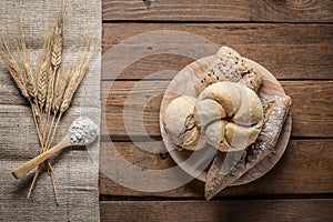 Bread with wheat ears and flour on wood board, top view