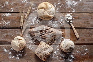 Bread with wheat ears and flour on wood board, top view