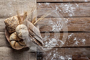 Bread with wheat ears and flour on wood board, top view