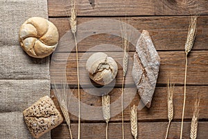 Bread with wheat ears and flour on wood board, top view
