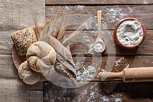 Bread with wheat ears and flour on wood board, top view