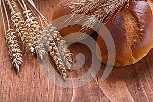 Bread with wheat ears on old wooden board