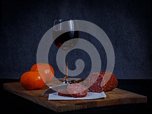 Breadboard with a sliced meat saucage a glass of red wine and two mandarins