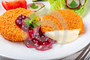Breaded and baked camembert with cranberry sauce on wooden tabel .
