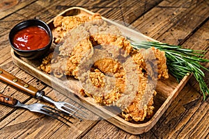 Breaded chicken breast tenders strips with ketchup. Wooden background. Top view