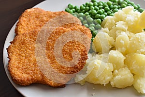 Breaded chicken escalope or chicken schnitzel with potatoes and green peas.
