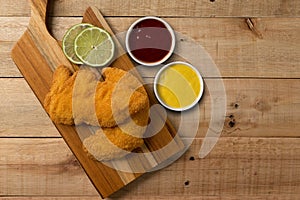 Breaded chicken filet, served with mustard and ketchup, on a wooden background. top wiew