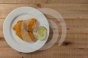 Breaded chicken fillet, served on a white plate, on wooden background. top wiew