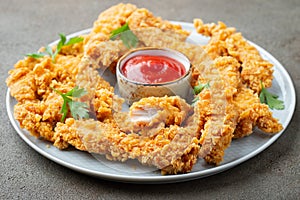 Breaded chicken strips with tomato ketchup on a white plate. Fast food on dark brown background