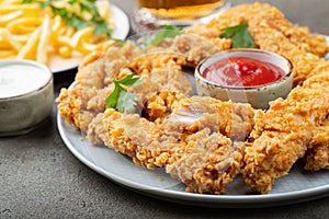 Breaded chicken strips with tomato ketchup on a white plate. Fast food on dark brown background photo
