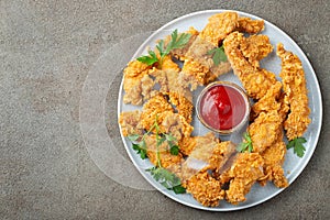 Breaded chicken strips with tomato ketchup on a white plate. Fast food on dark brown background. Top view with copy space