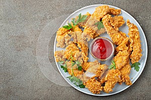 Breaded chicken strips with tomato ketchup on a white plate. Fast food on dark brown background. Top view with copy space photo