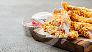 Breaded chicken strips with two kinds of sauces and fried potatoes on a wooden Board. Fast food on dark brown background. with cop