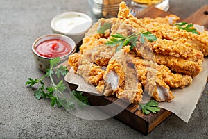 Breaded chicken strips with two kinds of sauces on a wooden Board. Fast food on dark brown background