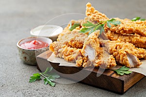 Breaded chicken strips with two kinds of sauces on a wooden Board. Fast food on dark brown background photo