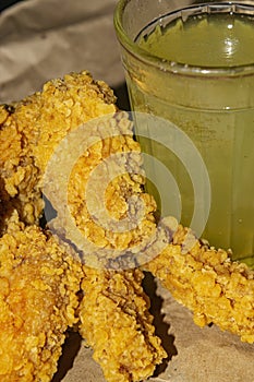 Breaded chicken wings and a glass of lemonade on a grey paper background. Close up