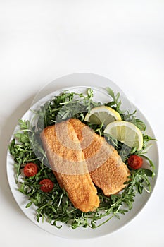 Breaded and fried fish fillets with salad and lemon.