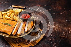 Breaded german weiner schnitzel with potato wedges. Dark background. Top view. Copy space