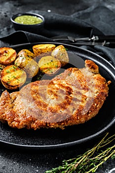 Breaded german weiner schnitzel with potatoes. Black background. Top view