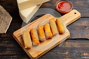 Breaded mozzarella cheese sticks with ketchup sauce on wooden cutting board