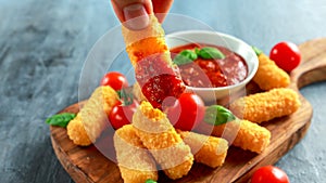 Breaded mozzarella cheese sticks in man hand with tomato basil sauce