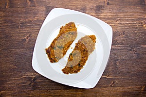 Breaded slices of meat on a plate on wood from above