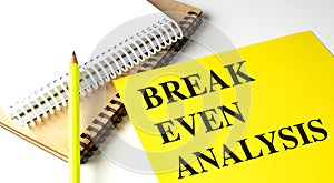 BREAK EVEN ANALYSIS text on yellow paper with notebooks