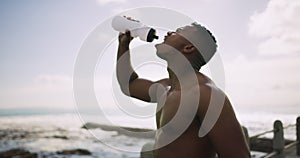 Break, fitness and a black man drinking water at the beach after running, cardio or exercise. Health, thirsty and an