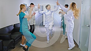 Break time in a modern hospital corridor doctors and nurses team dancing and smiling large feeling very excited and