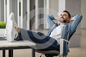 Break At Work. Young man relaxing at desk with legs on table