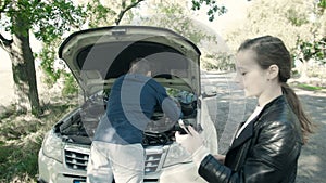 Breakdown of the car on the road. The daughter gives a wrench to the father, repairing the engine.