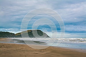 Breakers rolling over vast sand beach. Thick mist over ocean beach on a stormy day. Makorori beach, Gisborne, North