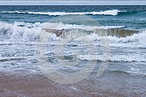 Breakers rushing onto the shore with spray and foam on a stormy day at the beach