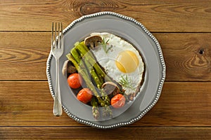 Breakfast with asparagus, fried egg and cherry tomatoes. Wooden table