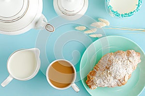 Breakfast background. Fresh croissants on turquoise plates, milk and coffee on pastel blue table. Top view