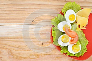Breakfast background. Hard boiled eggs, sliced in halves, salad, tomatoes and cheese on the red plate.
