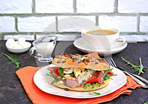 Breakfast, bagel with scramble egg, ham, arugula and vegetables on a white plate