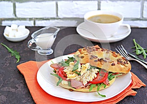 Breakfast, bagel with scramble egg, ham, arugula and vegetables on a white plate