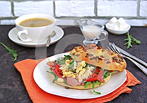 Breakfast, bagel with scramble egg, ham, arugula and vegetables on a white plate