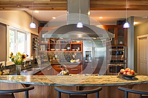 Breakfast bar in contemporary upscale home kitchen interior with granite countertops, vent hood and accent lighting