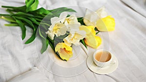 Breakfast in bed. A bouquet of tulips lies on the bed next to a cup of hot coffee. Spring. Gift. Good morning