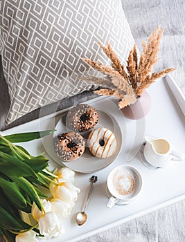Breakfast in bed, cup with cappuccino, doughnuts, flowers white tulips