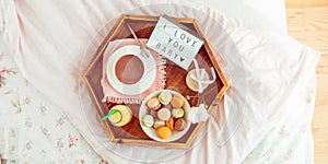 Breakfast in bed with I love you baby text on lighted box. Cup of coffee, juice, macaroons, flower and gift box on wooden tray.