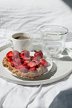 Breakfast in bed with morning sunlight. Elegant tray with toast and fresh strawberries, coffee and morning glass of water laying o