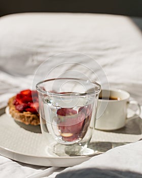 Breakfast in bed with morning sunlight. Elegant tray with toast and fresh strawberries, coffee and morning glass of water laying o