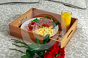 Breakfast in bed on wooden tray with bunch of red roses. Scrumbled eggs, fried bacon, beans on toast and salad, with