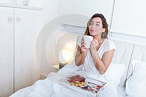 Breakfast in bed for young beautiful woman. Woman having coffee and breakfast in bed with fruits, coffee and biscuits. Morning