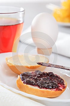 Breakfast with boiled egg, French bun, jam, tea and butter. The knife smears jam.