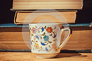 Breakfast of bookworm with vintage books and floral design cup of coffee. Selective focus