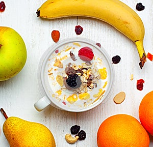 Breakfast with bowl of milk, cereals and red fruits on white table and fresh fruit